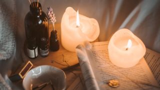 lighted candle on white book beside black glass bottle