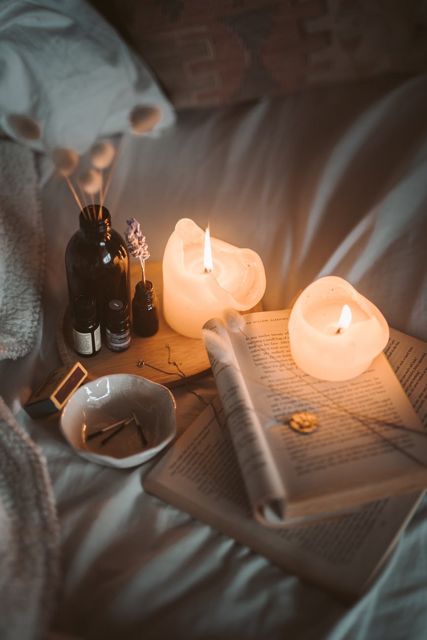 lighted candle on white book beside black glass bottle